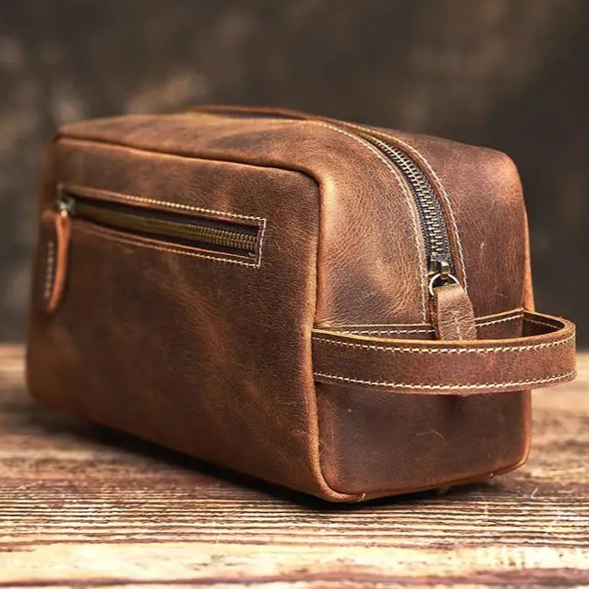 Trousse de toilette homme en cuir marron vintage posée sur une table en bois, format compact 24x13x10 cm
